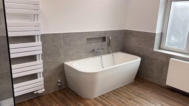 Vorwandbadewanne mit gefliester Ablagenische, Fliesen in Betonoptik und Boden in Holzoptik