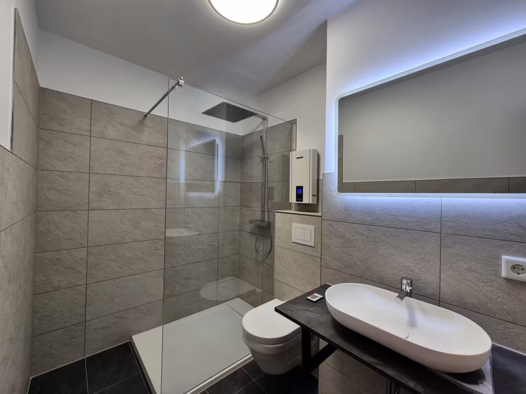 Bad in Steinoptik mit Walk-in-Dusche, wandhängendem WC und LED-Lichtspiegel