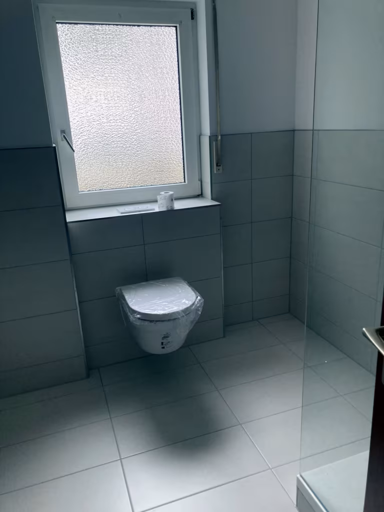 Wandhängendes WC unter dem Fenster, großformatige Fliesen in Hellgrau und Weiß